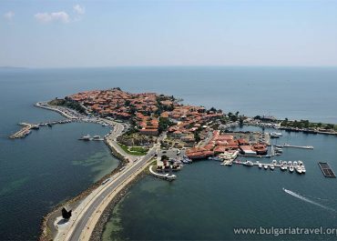 Bird's eye view of a small coastal town featuring charming architecture, sandy beaches, and boats in the bay.