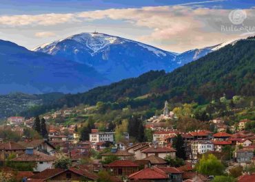 a city with red roofs and trees and mountains in the background