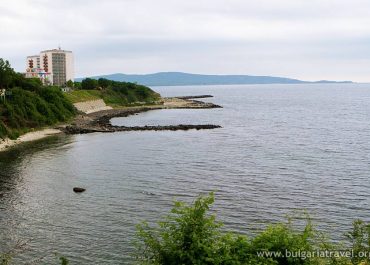 Scenic sea view from hilltop, waves gently crashing on shore, clear blue sky above.